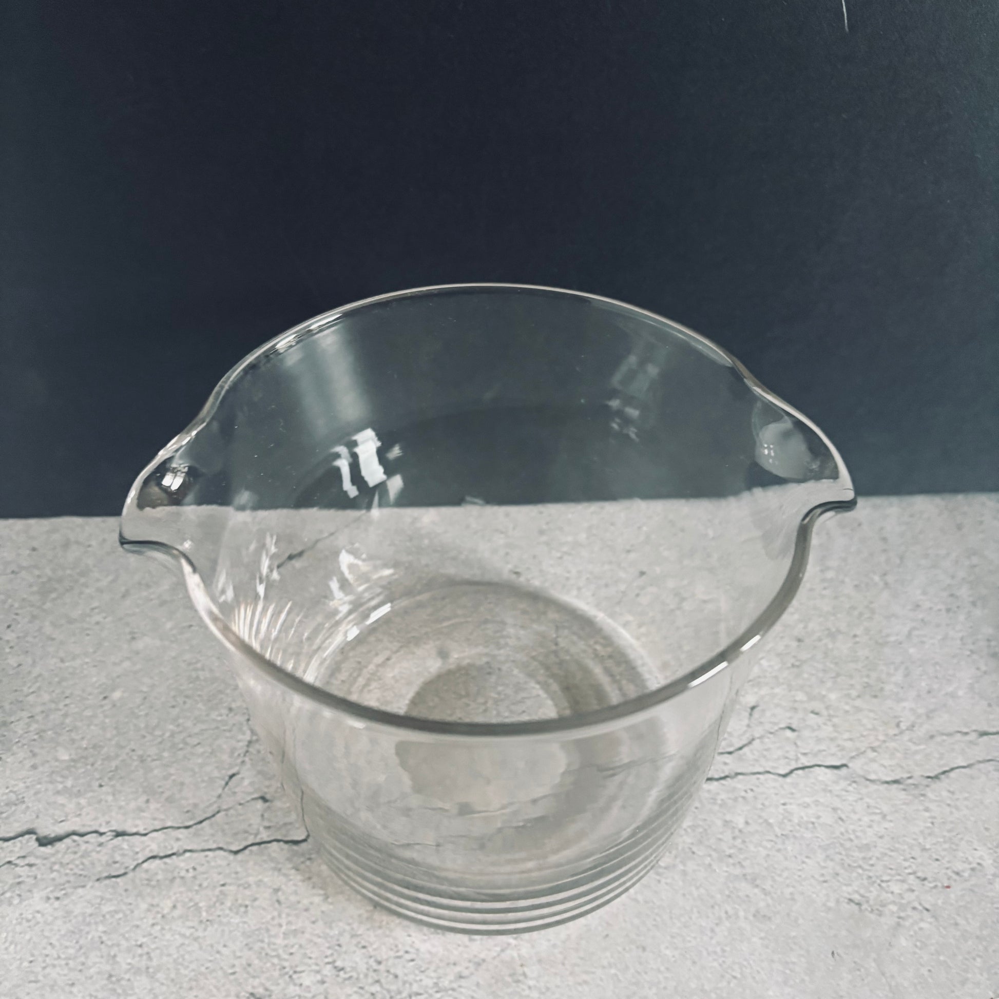Clear glass beaker on a gray surface with a dark background