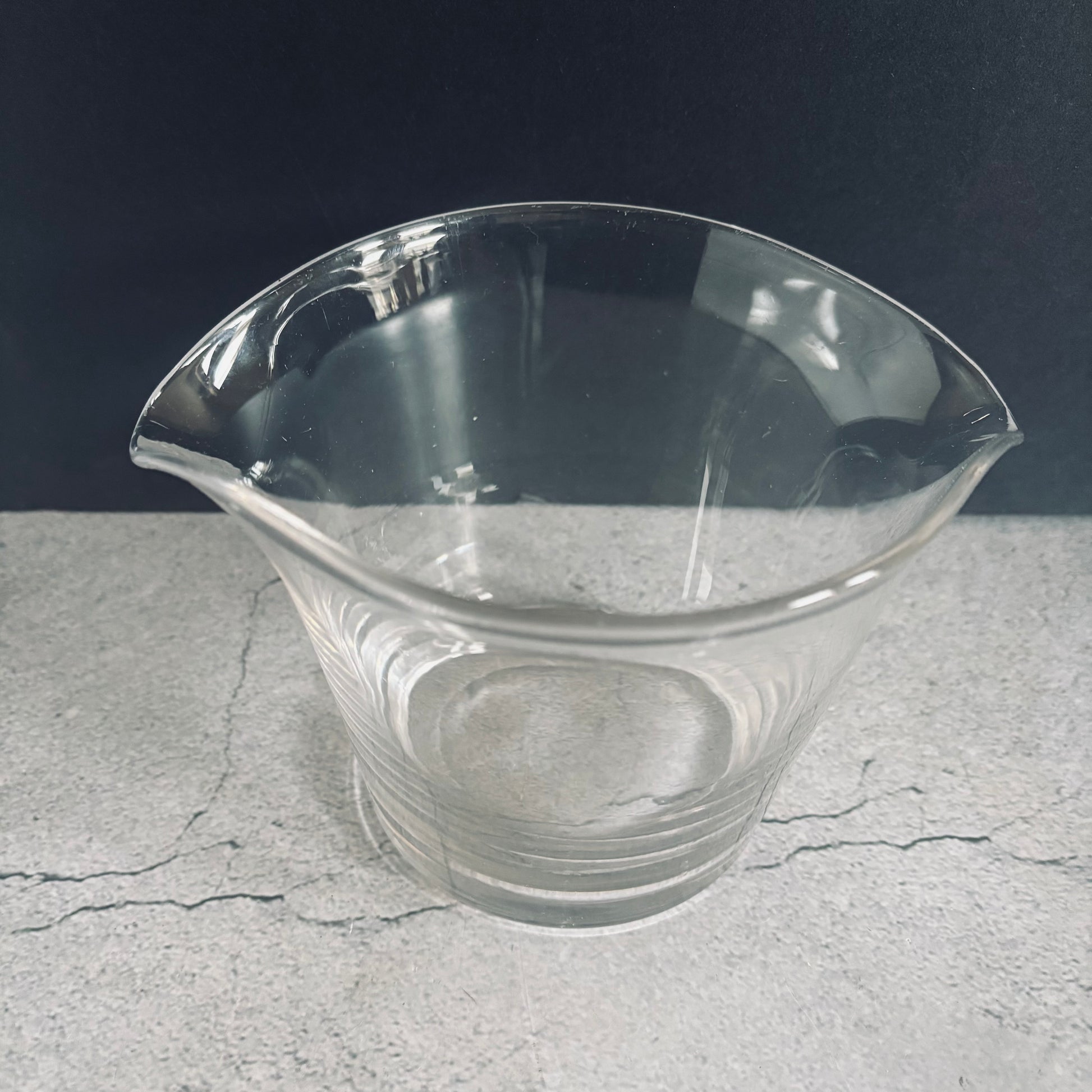 a clear glass antique cooling rinser on a textured gray surface with a dark background