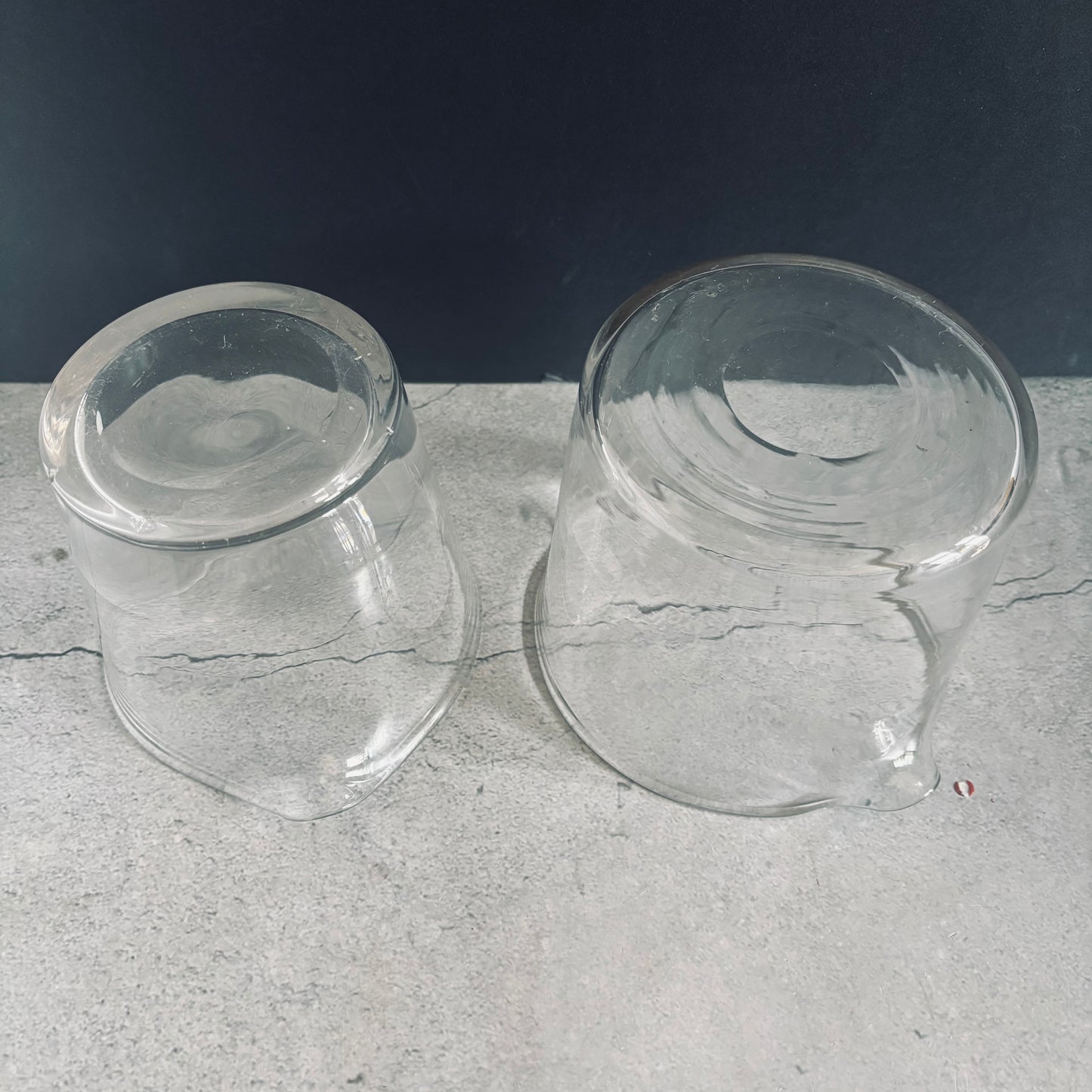 underside of two clear glass antique cooling rinsers on a textured grey surface with a dark background