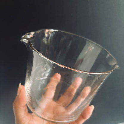 Clear glass rinser held by a hand against a dark background