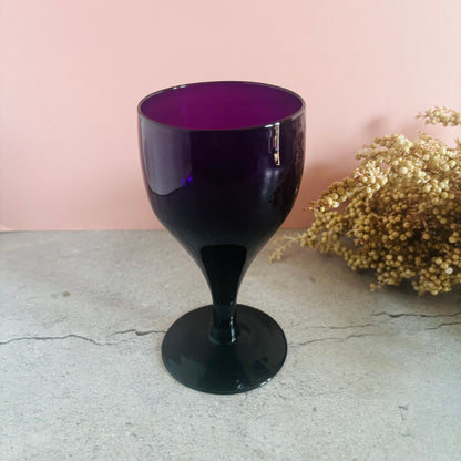 Amethyst wine glass with purple interior on a light gray surface with a pink background and dried flowers.
