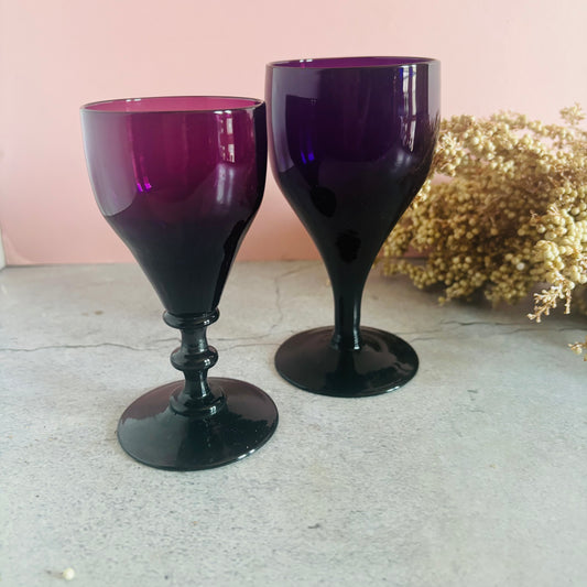 Two purple wine glasses on a light surface with a blurred background