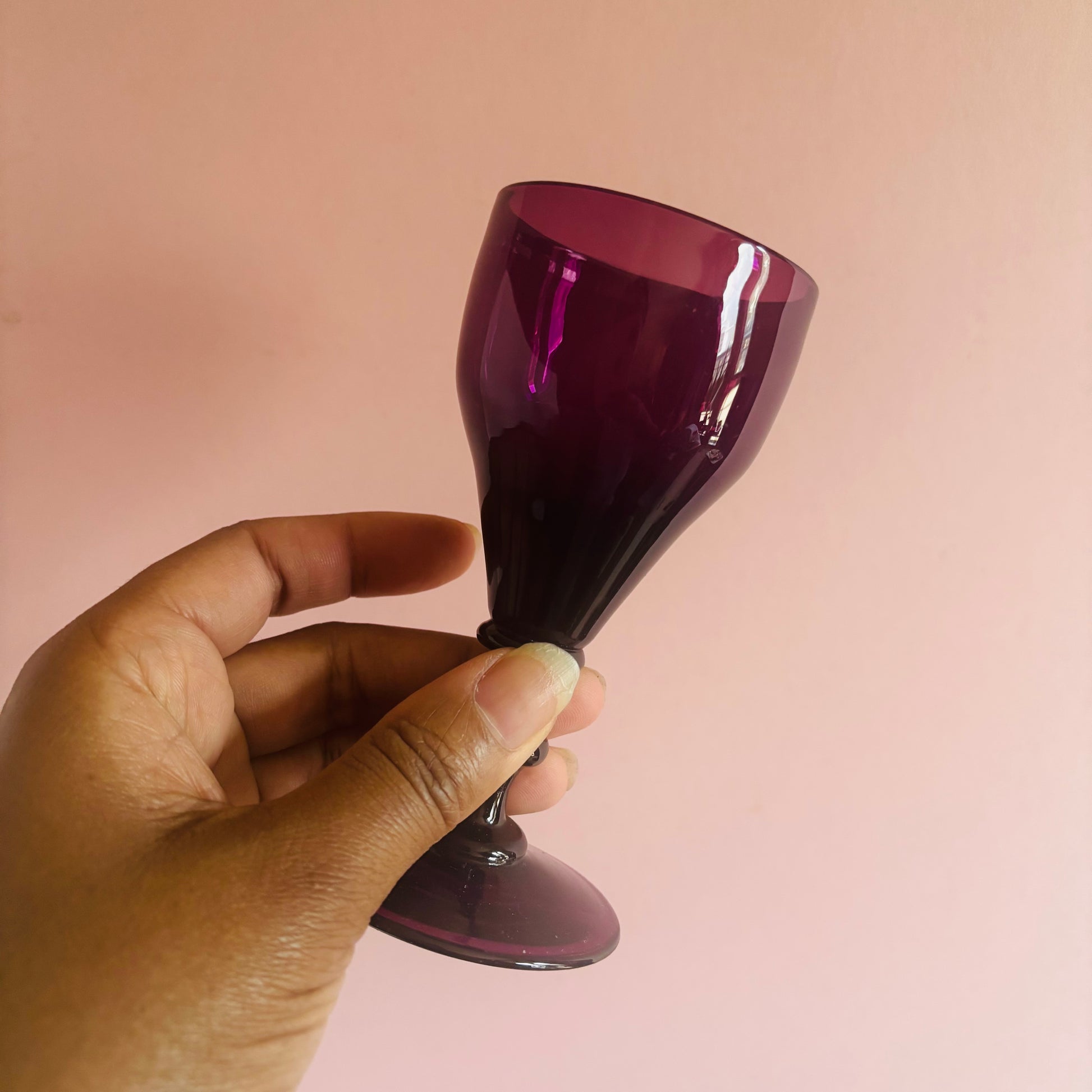Hand holding a purple glass against a pink background