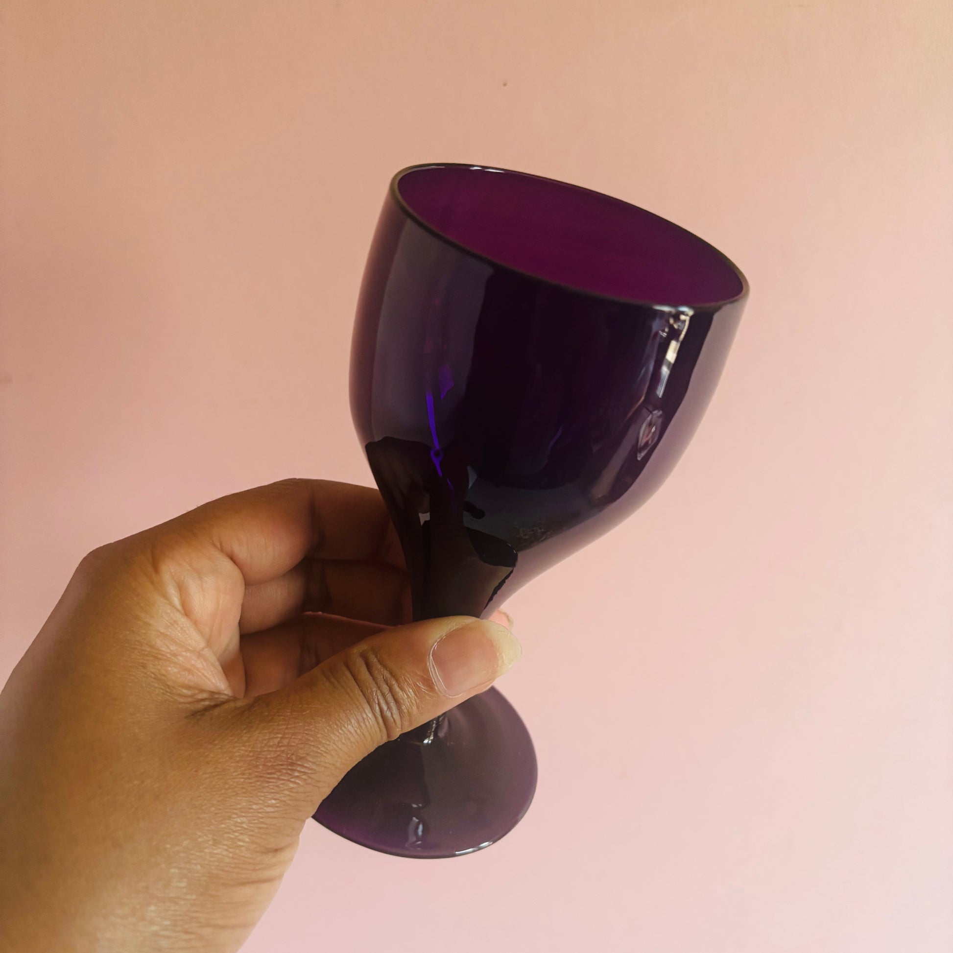 Hand holding a dark purple object against a pink background