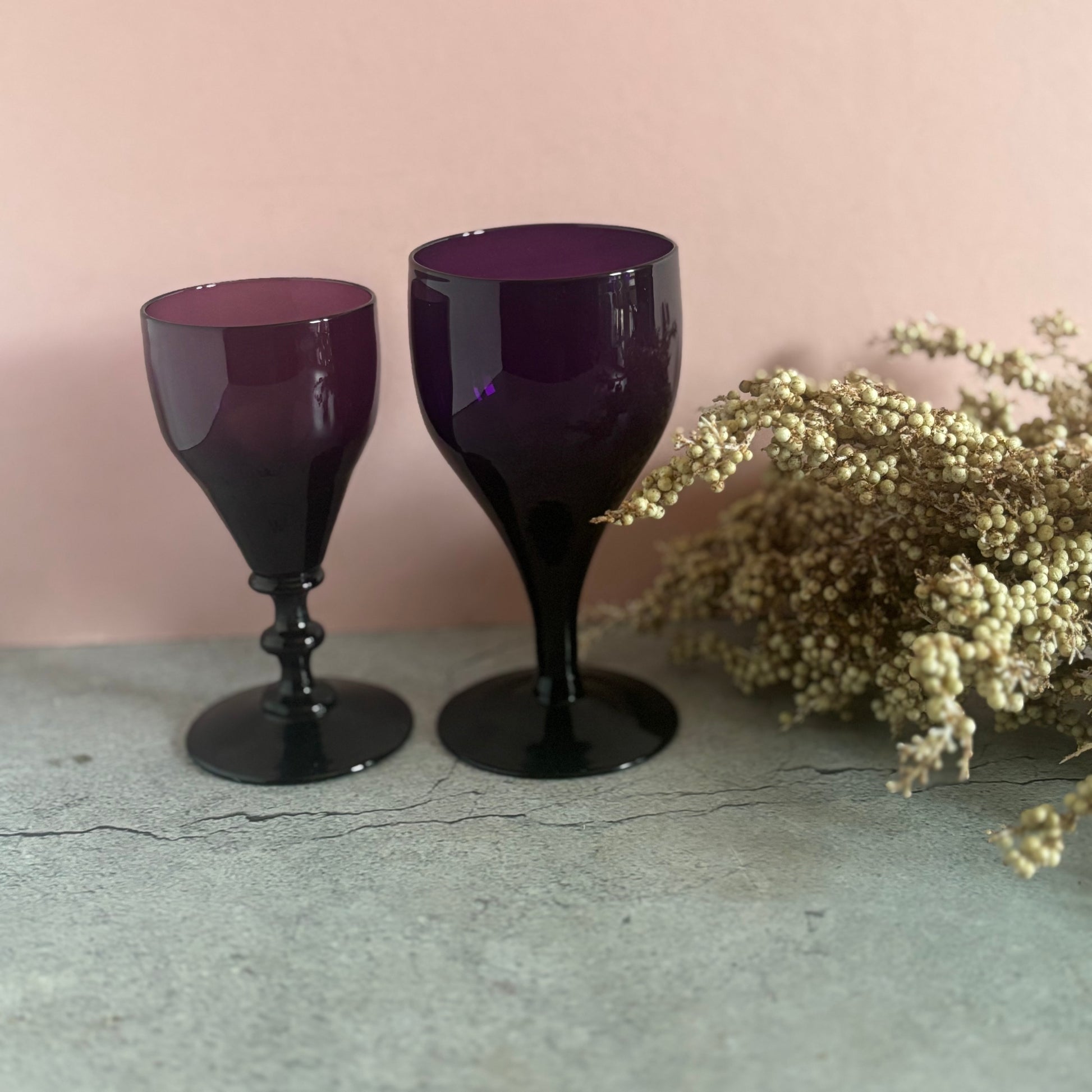 Two purple goblets on a textured surface with a light pink background