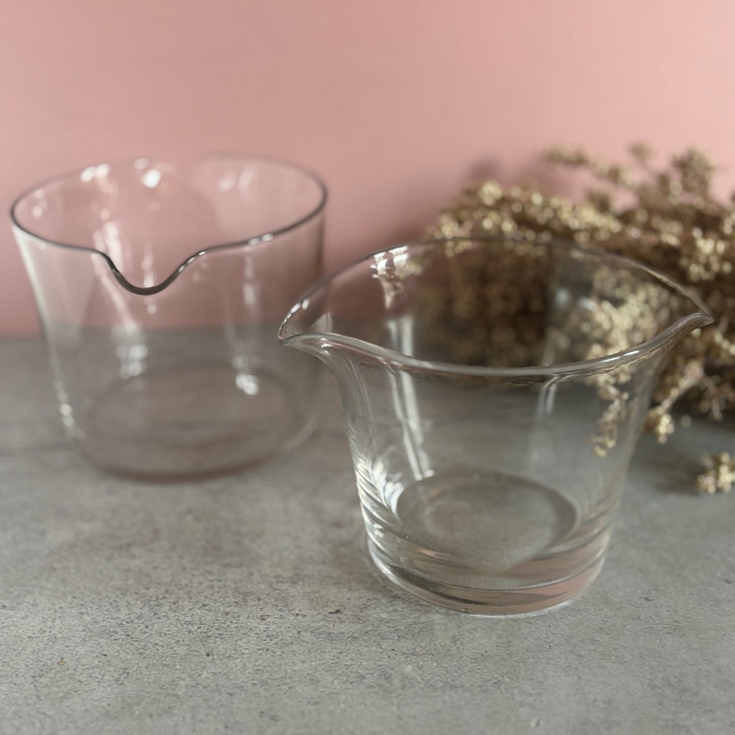 Two clear glass rinsers on a gray surface with a pink background