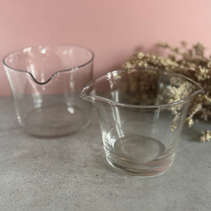 Two clear glass rinsers on a gray surface with a pink background