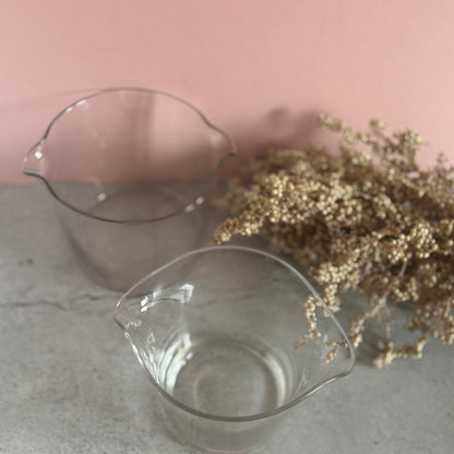 Two clear glass antique cooling rinsers on a textured surface with a pink background
