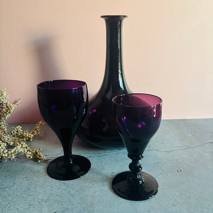 Two purple goblets and a tall black vase on a light surface with a neutral background.