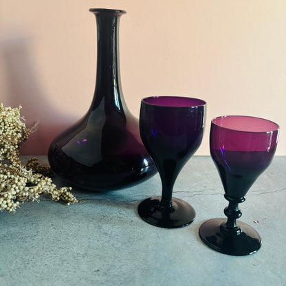 Two purple glass goblets and a black vase on a textured surface with a neutral background.