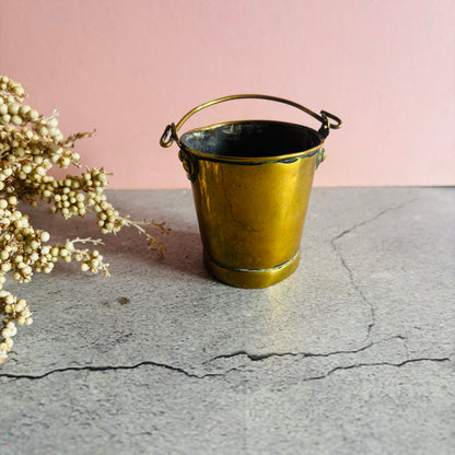 Edwardian Novelty Brass Bucket Vesta match safe on a stone surface against a pink wall