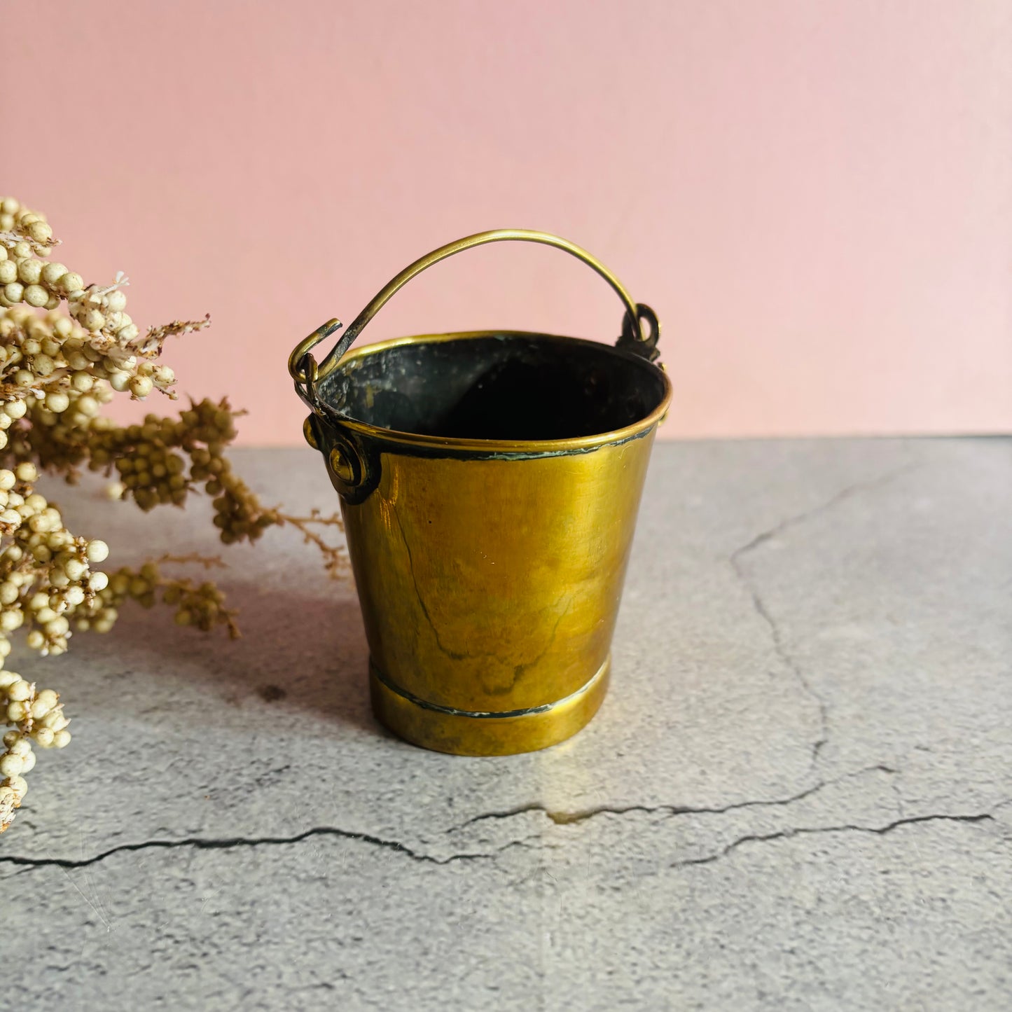 Brass bucket on a textured surface with a pink background