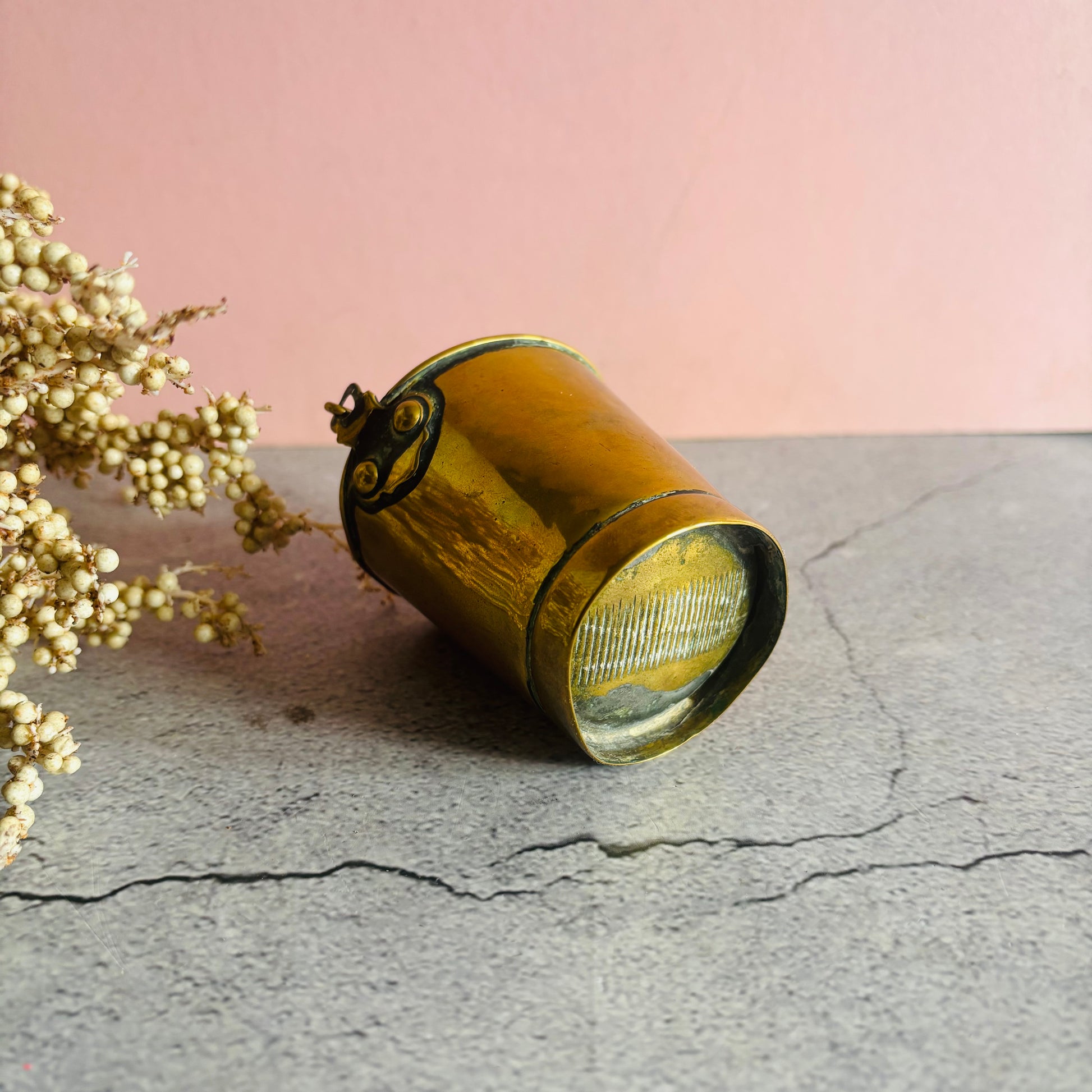 Antique Novelty Brass Bucket Vesta on a stone surface against a pink wall