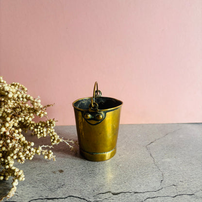 Edwardian Novelty Brass Bucket Vesta on a stone surface against a pink wall