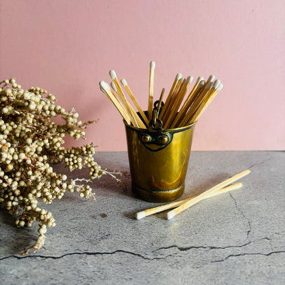 Edwardian Novelty Brass Bucket Vesta with matchsticks on a stone surface against a pink wall