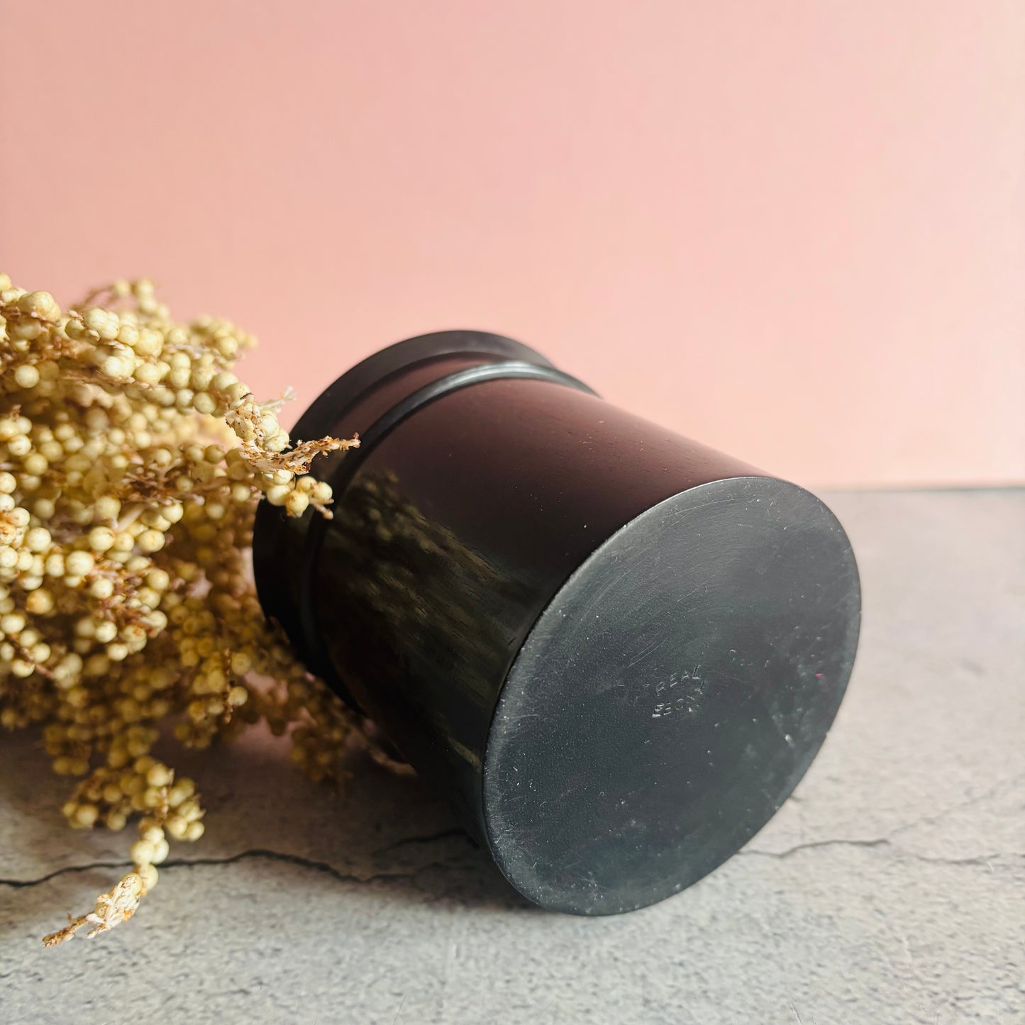 Black cylindrical container with dried flowers on a light pink background
