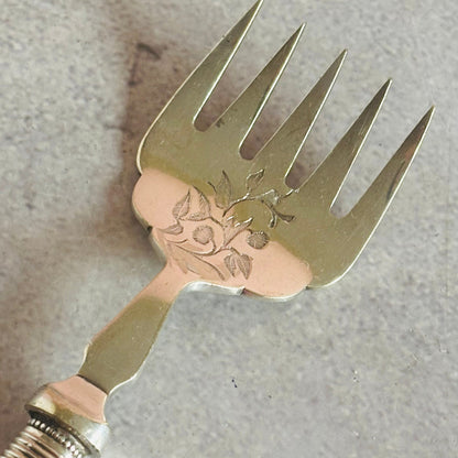 Decorative metal fork with floral engraving on a gray background