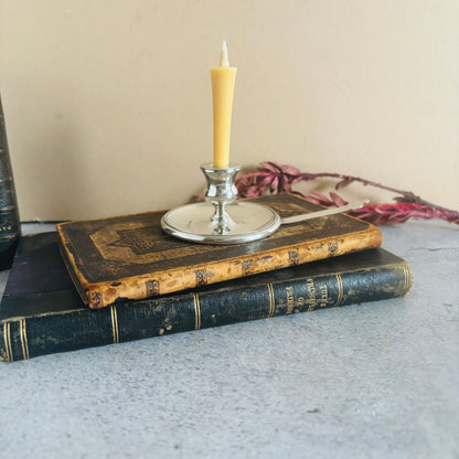 Two old books stacked with a candle in a holder on top, on a textured surface.
