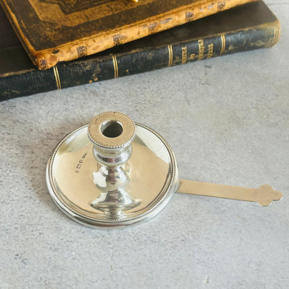 Antique Silver Go To Bed Candlestick on a textured surface with old books in the background