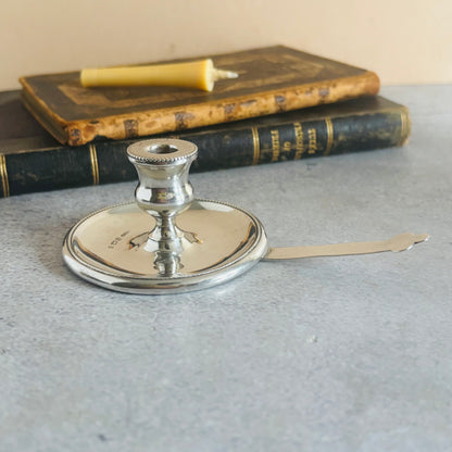 Silver candlestick holder on a textured surface with books in the background