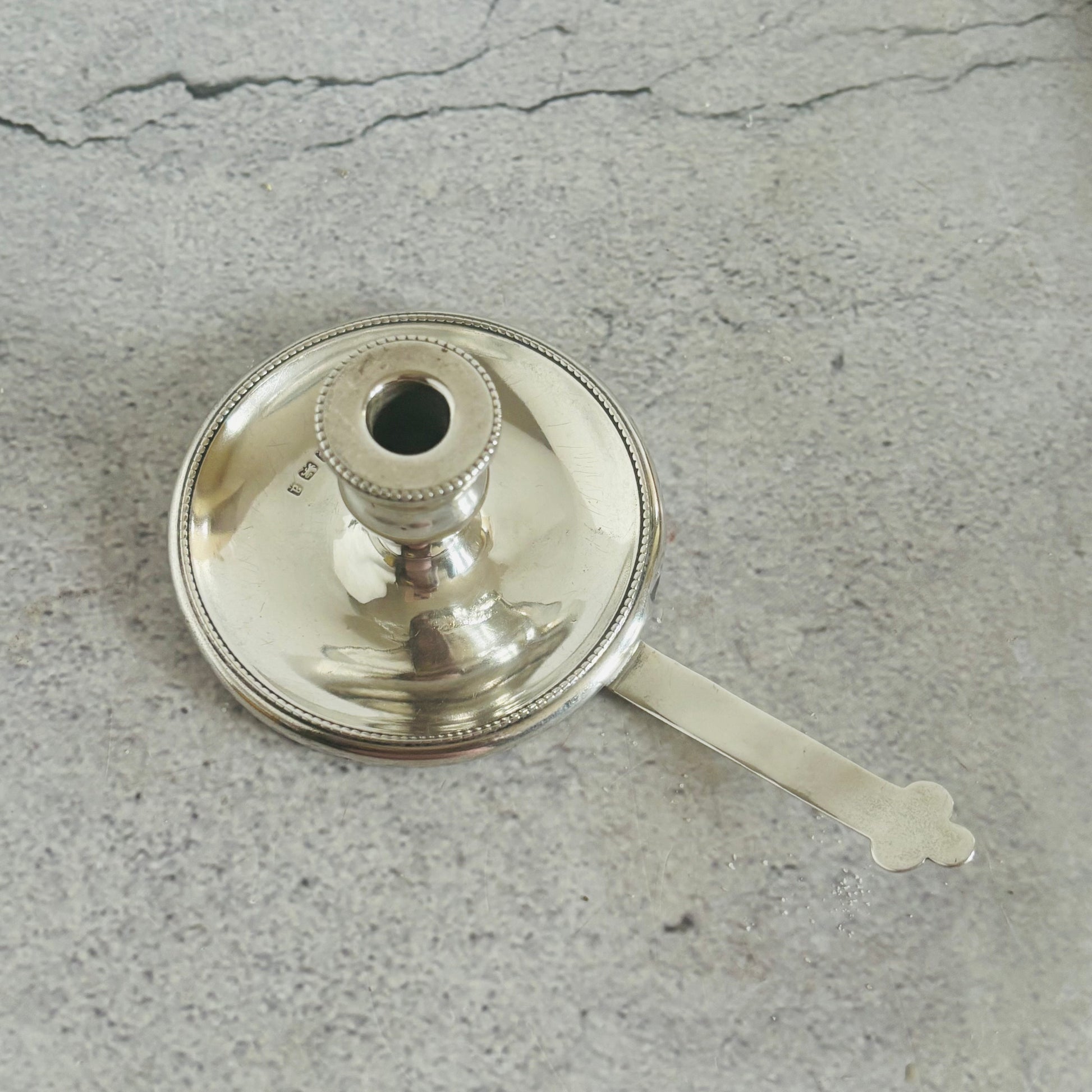 Silver candle holder with a handle on a gray surface