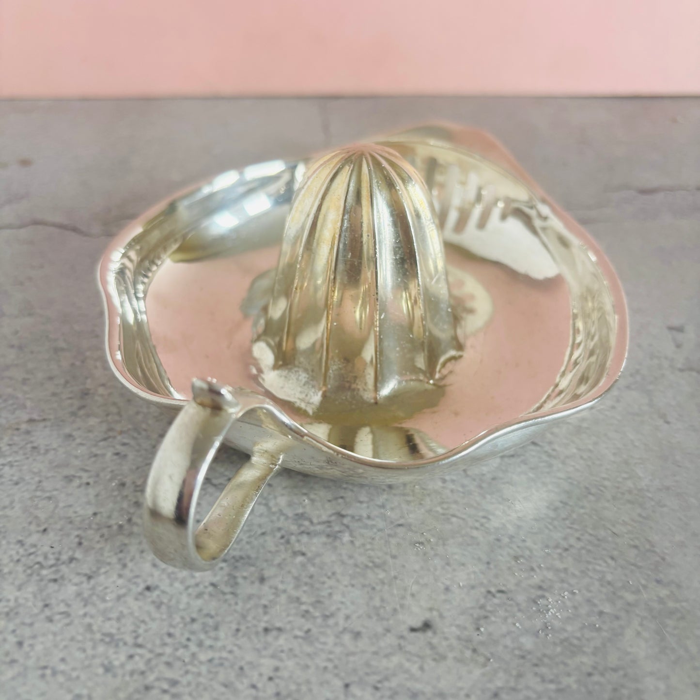 Silver lemon squeezer on a gray surface with a pink background