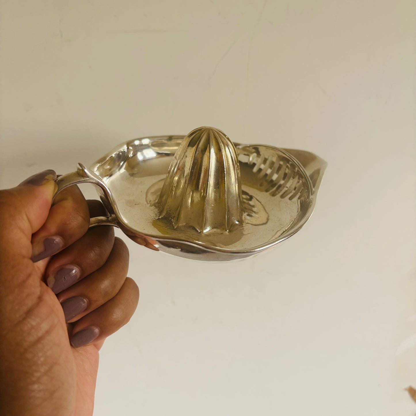 Hand holding a silver manual juicer against a plain background