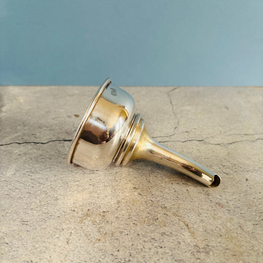 A polished slver funnel lying on its side on a textured stone surface with a blue background.