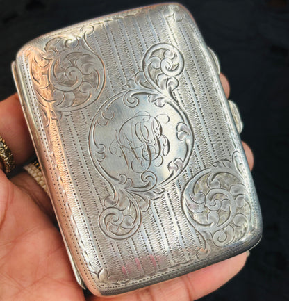 Silver cigarette case with intricate engravings held in a hand against a dark background