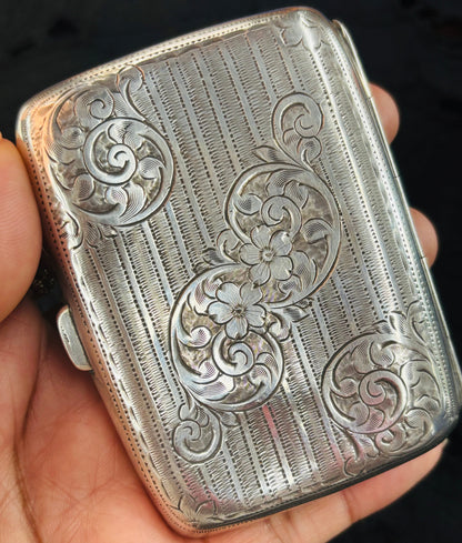 Silver embossed cigarette case held in a hand against a dark background