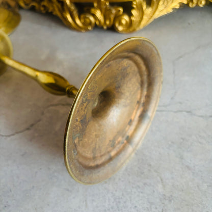Close-up of a vintage brass candelabra base and stem, showing aged gold and bronze patina details on a light gray stone surface.