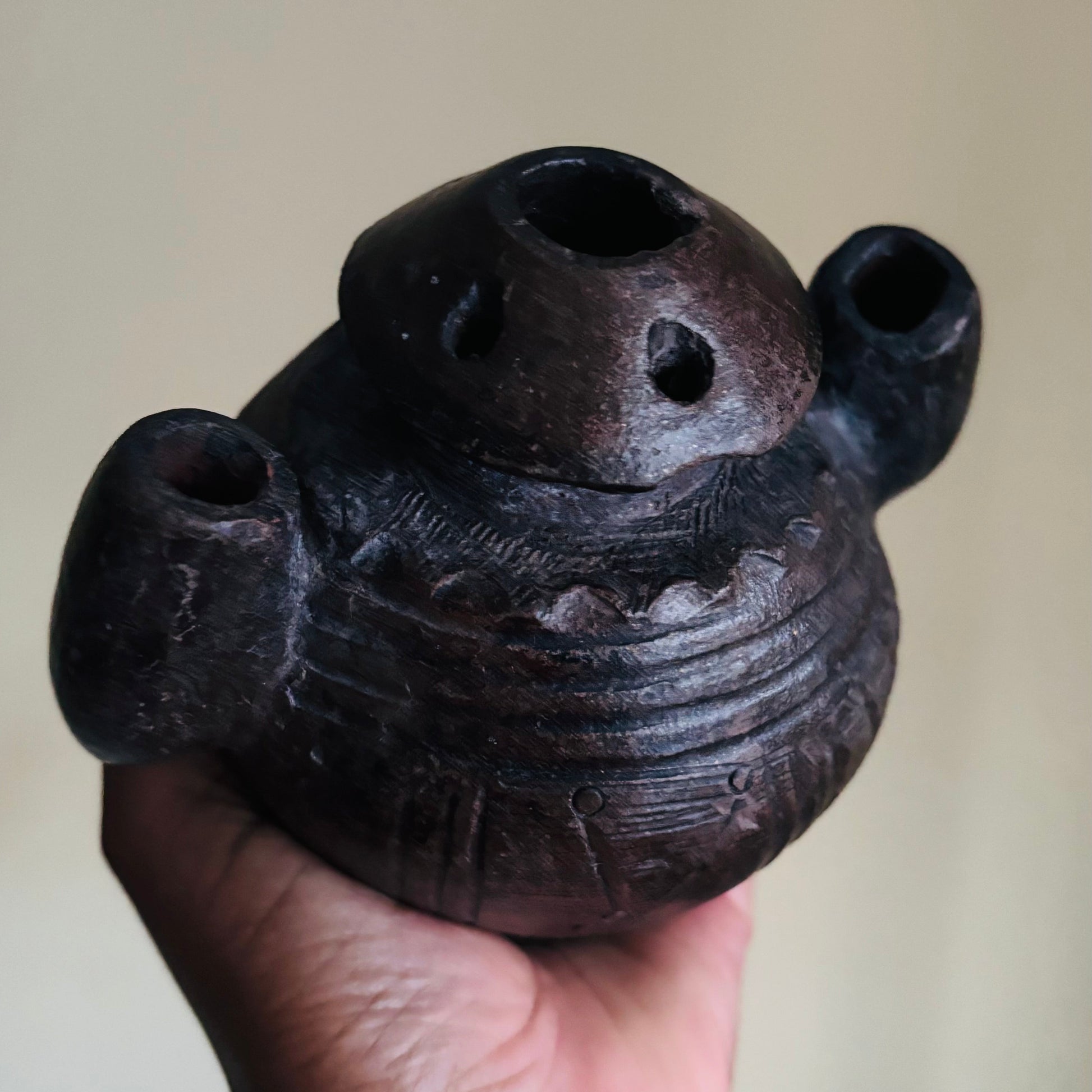 Hand holding Antique African Clay Ink Pot From Kano Nigeria with multiple holes against a neutral background
