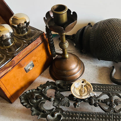 Collection of vintage metal objects including a candlestick and ornate pieces on a textured surface.