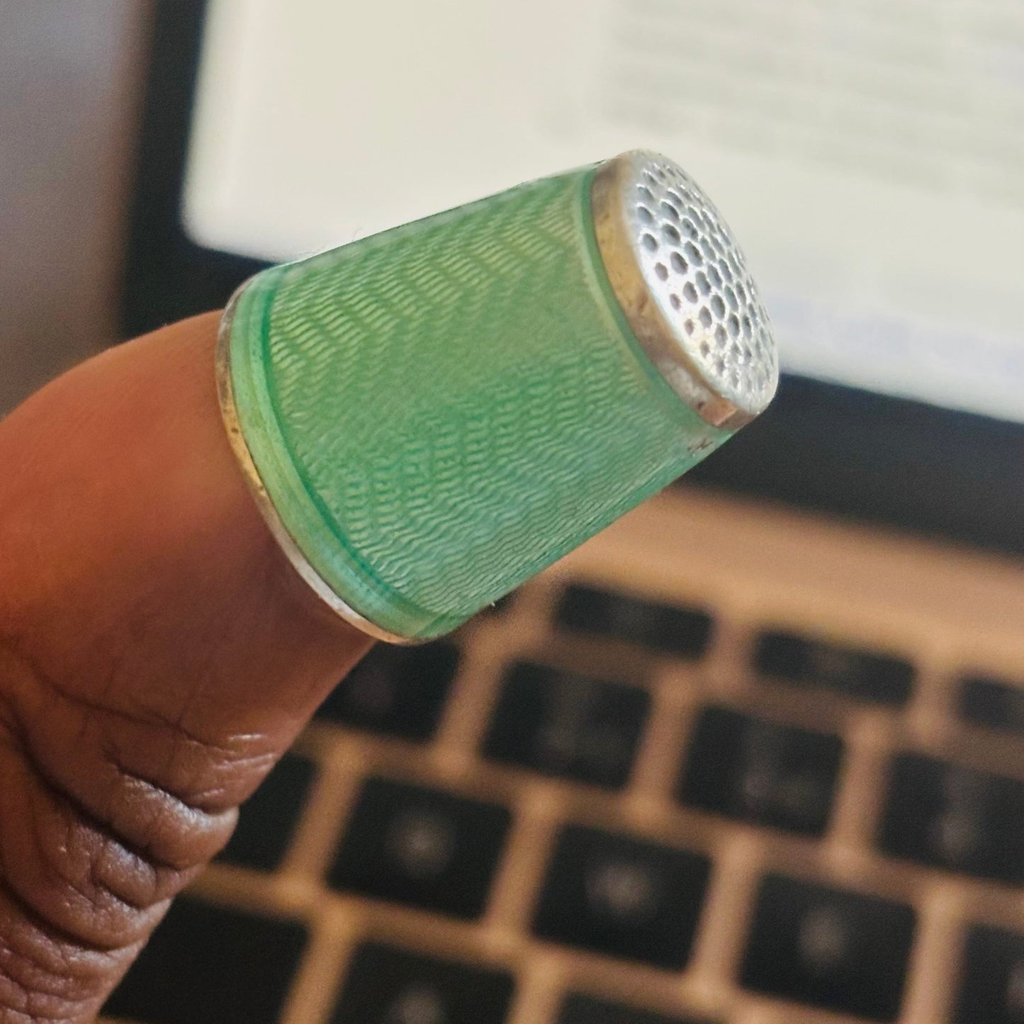 Green thumb sleeve on a finger with a laptop keyboard in the background