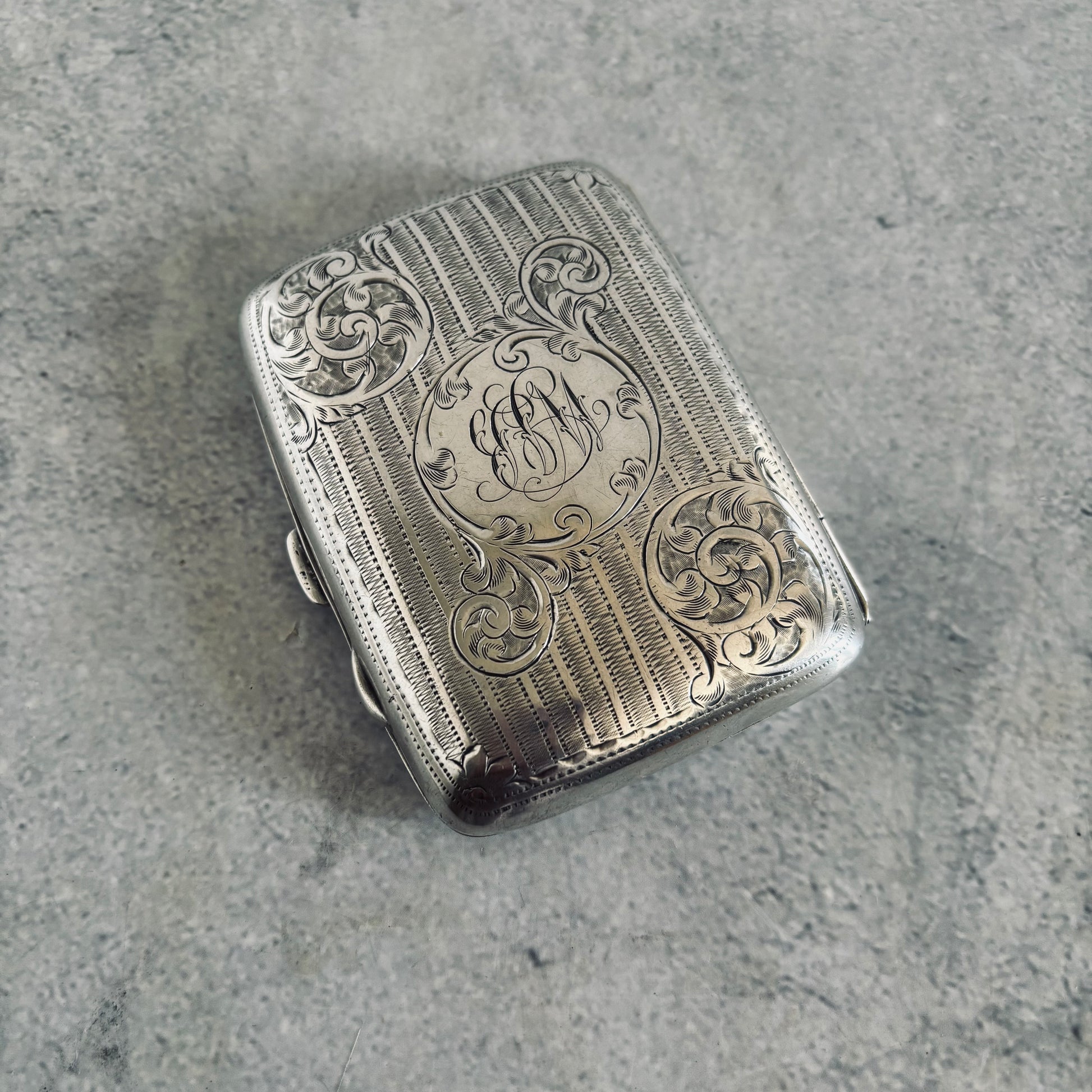 Silver cigarette case with intricate engravings on a gray surface