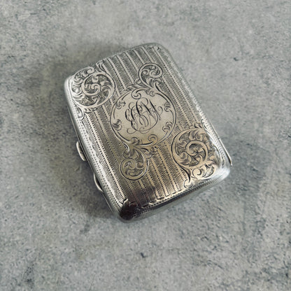 Silver cigarette case with intricate engravings on a gray surface