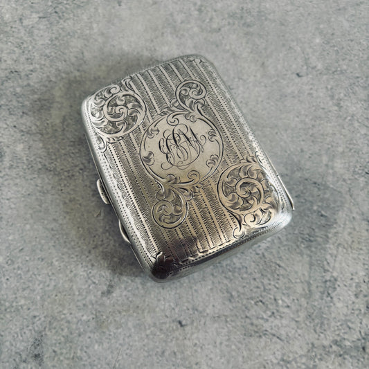 Silver cigarette case with intricate engravings on a gray surface