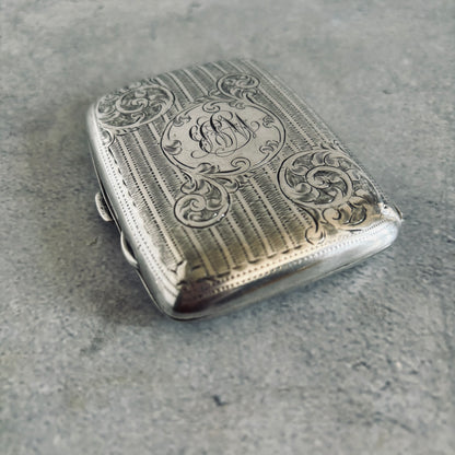 Silver cigarette case with intricate engravings on a gray surface