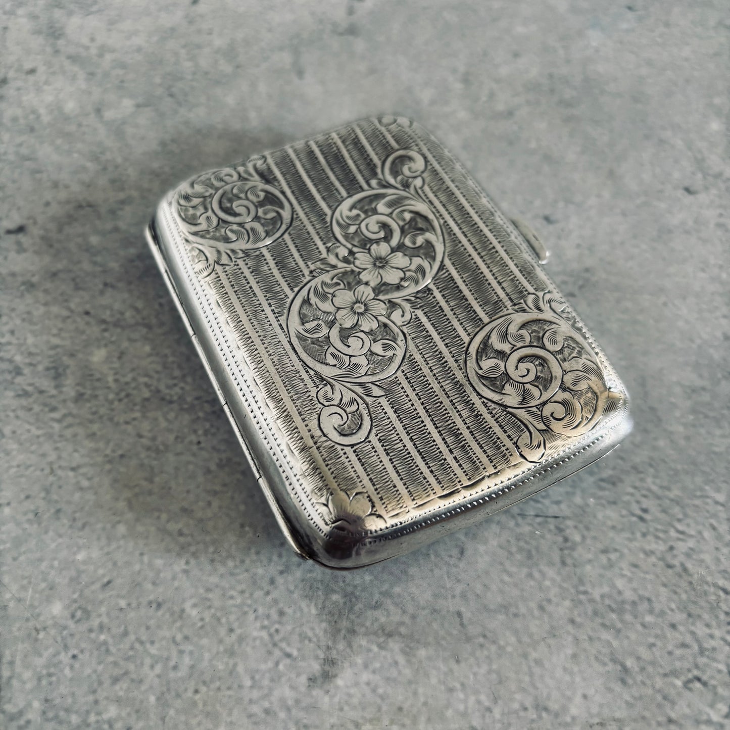 Silver cigarette case with intricate engravings on a gray surface