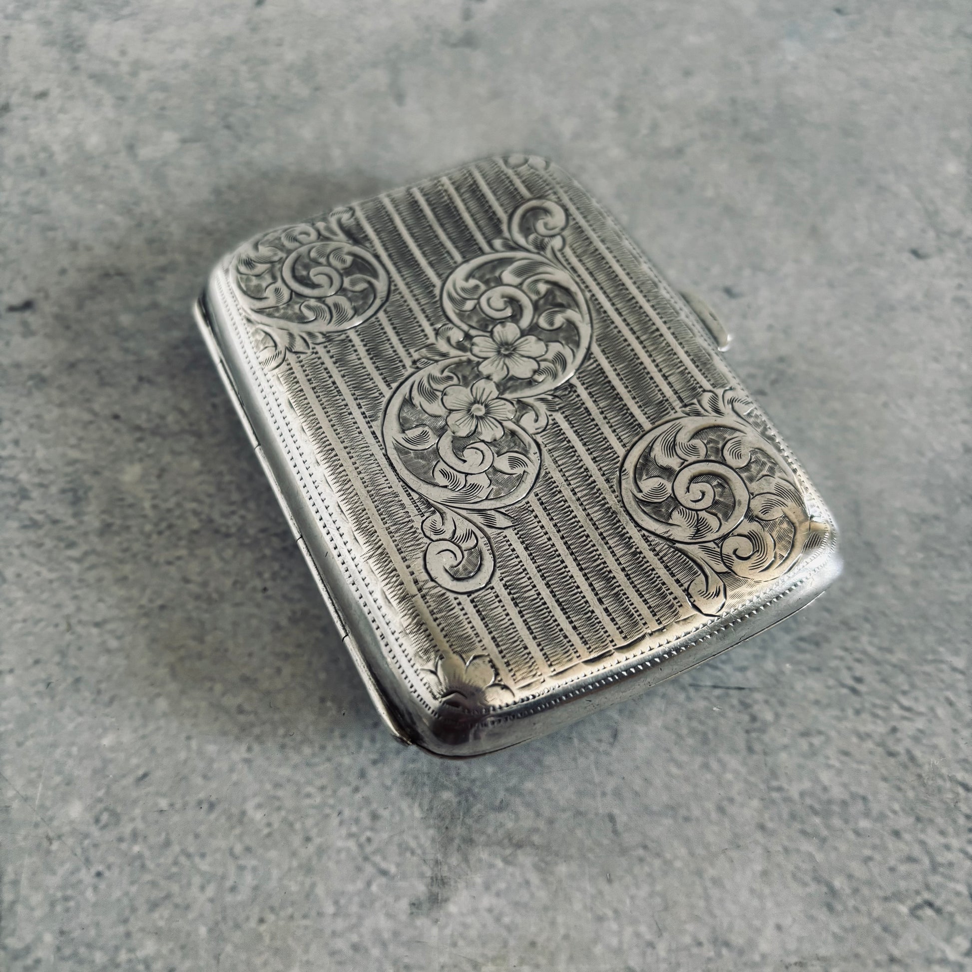 Silver cigarette case with intricate engravings on a gray surface