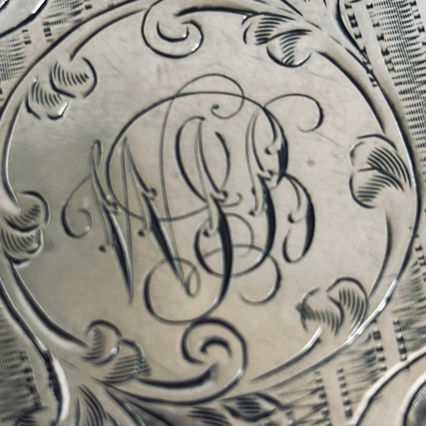 Close-up of a silver coin with engraved initials and decorative patterns