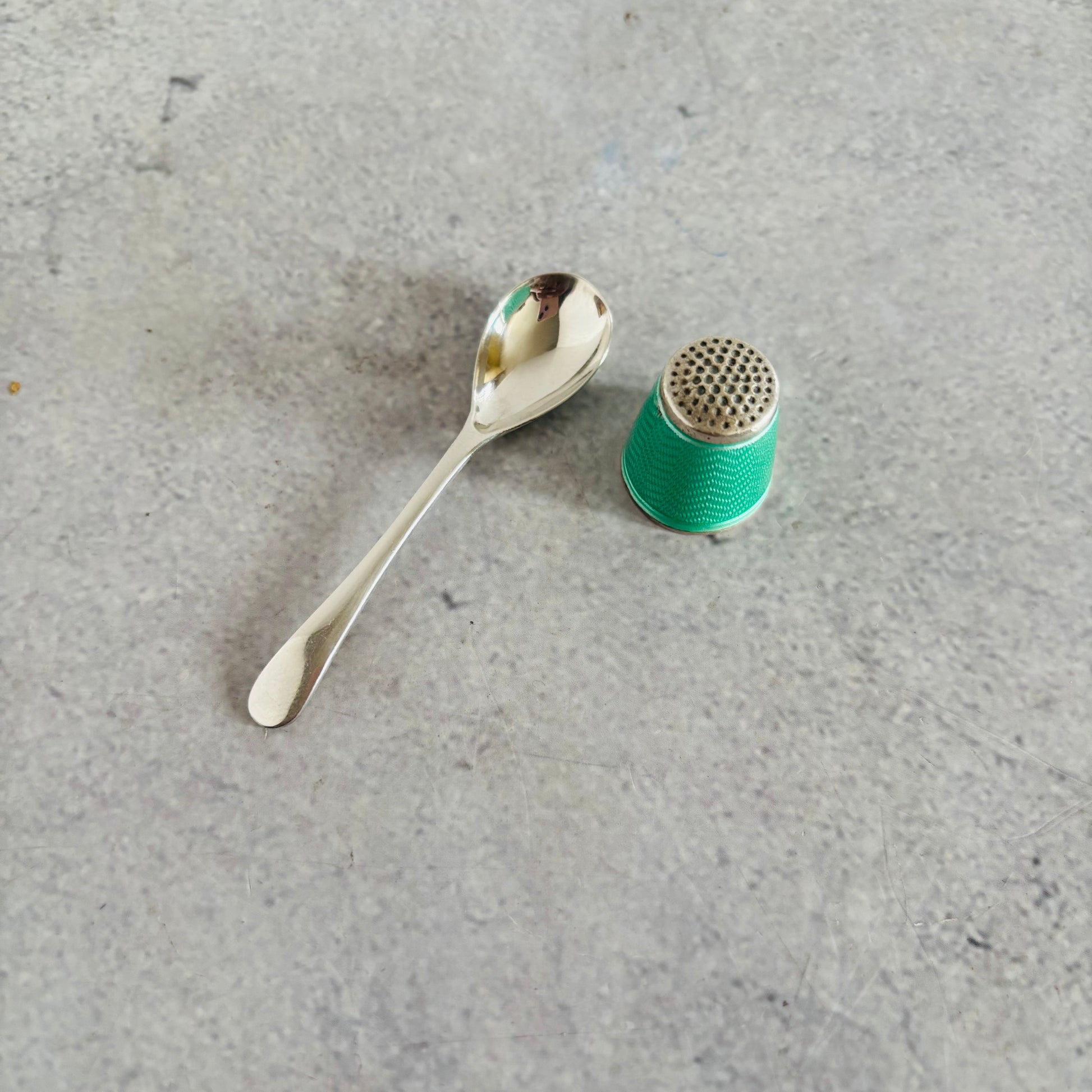 Silver spoon and green thimble on a gray concrete surface