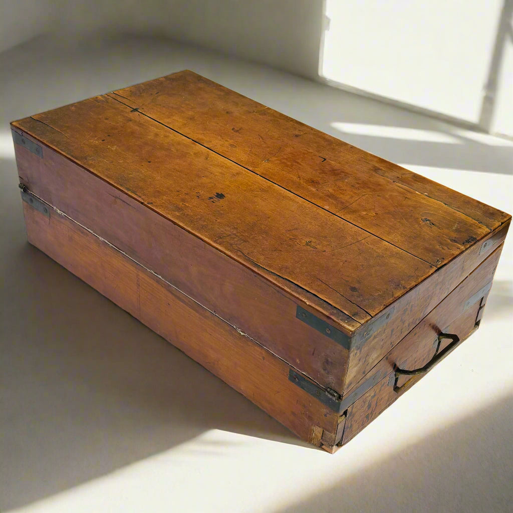 Vintage wooden trunk on a white surface with sunlight casting shadows.