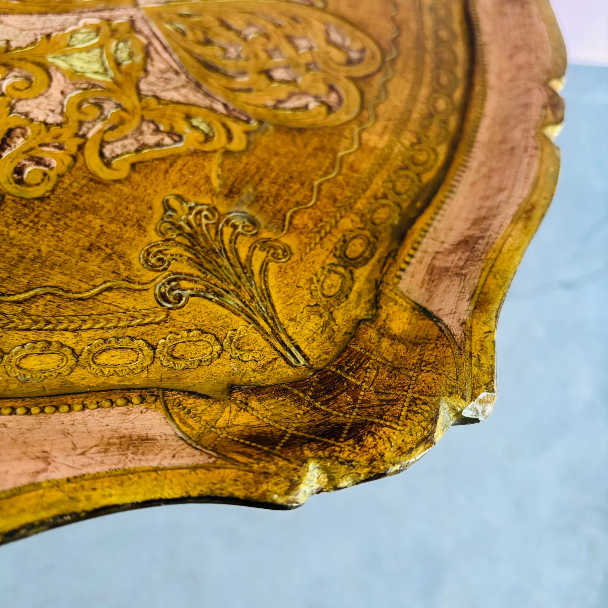 Close-up of a vintage florentine tray surface with intricate carvings on a light blue background