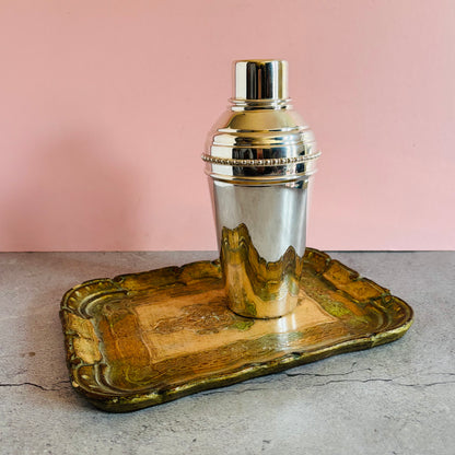 Silver cocktail shaker on a decorative wooden tray with a pink background