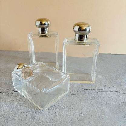 Three clear glass perfume bottles with silver tone caps on a grey surface.
