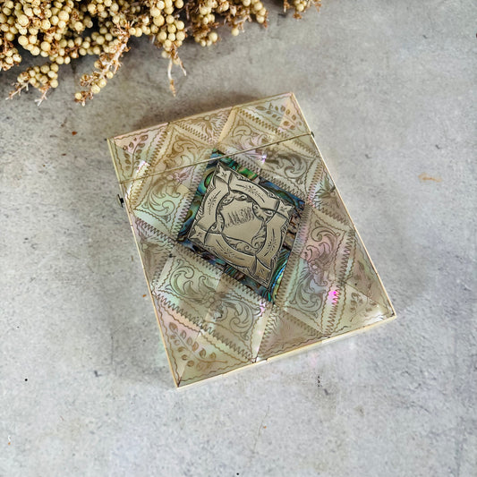 A Rare Antique Mother Of Pearl And Sterling Silver Calling Card Case, photographed from above on a light grey concrete surface with dried flowers in the corner.
