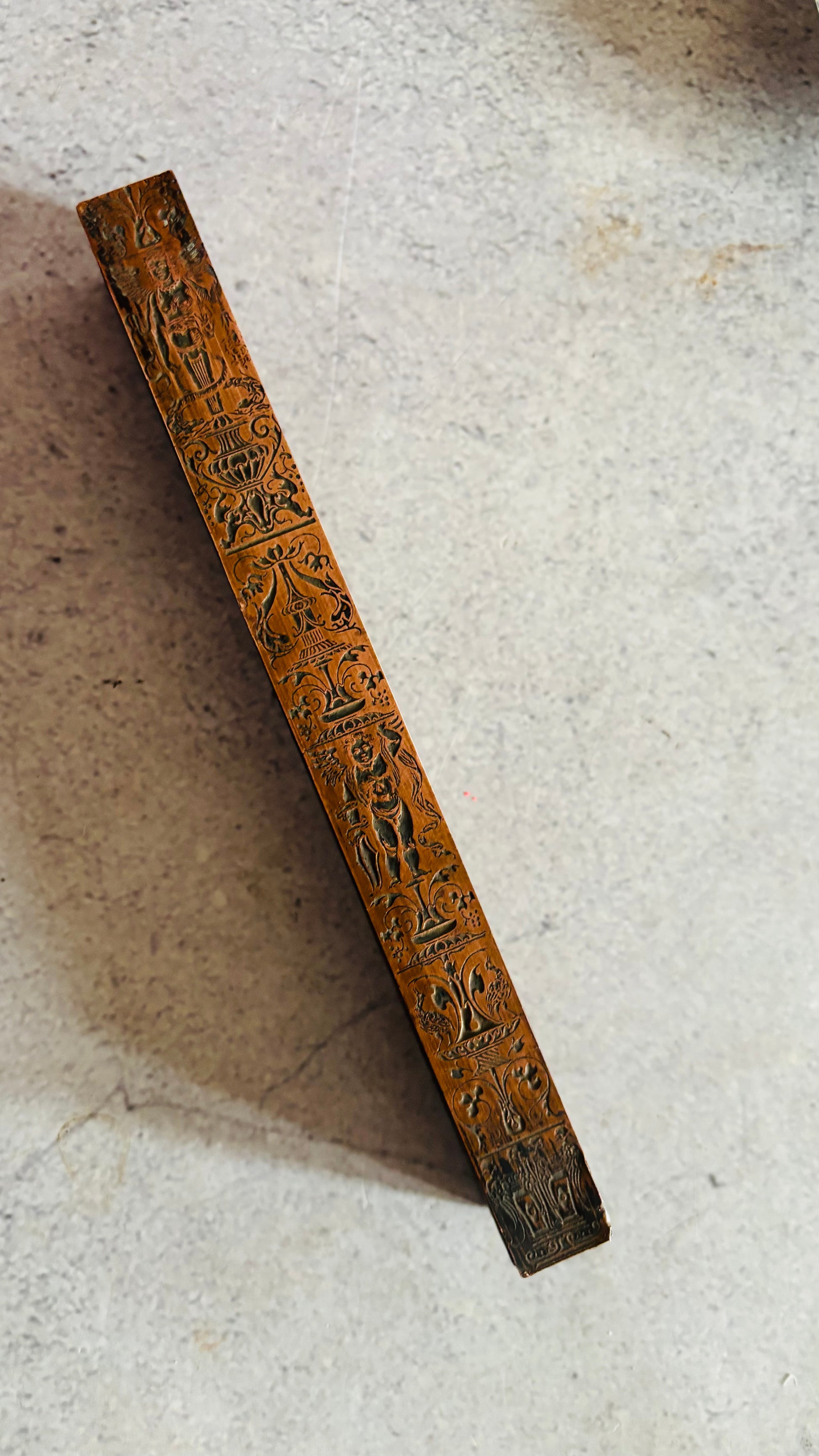 Decorative copper and wooden block with intricate carvings on a light grey background