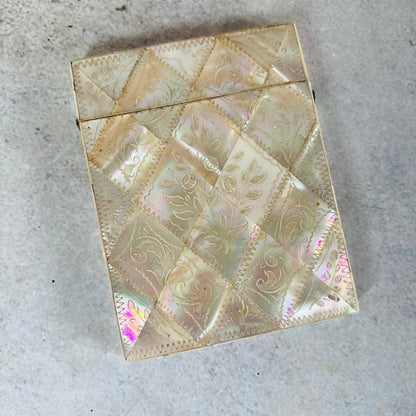 A vintage iridescent shell-covered card case with a diamond quilted pattern and embossed floral motifs, photographed on a textured gray surface.