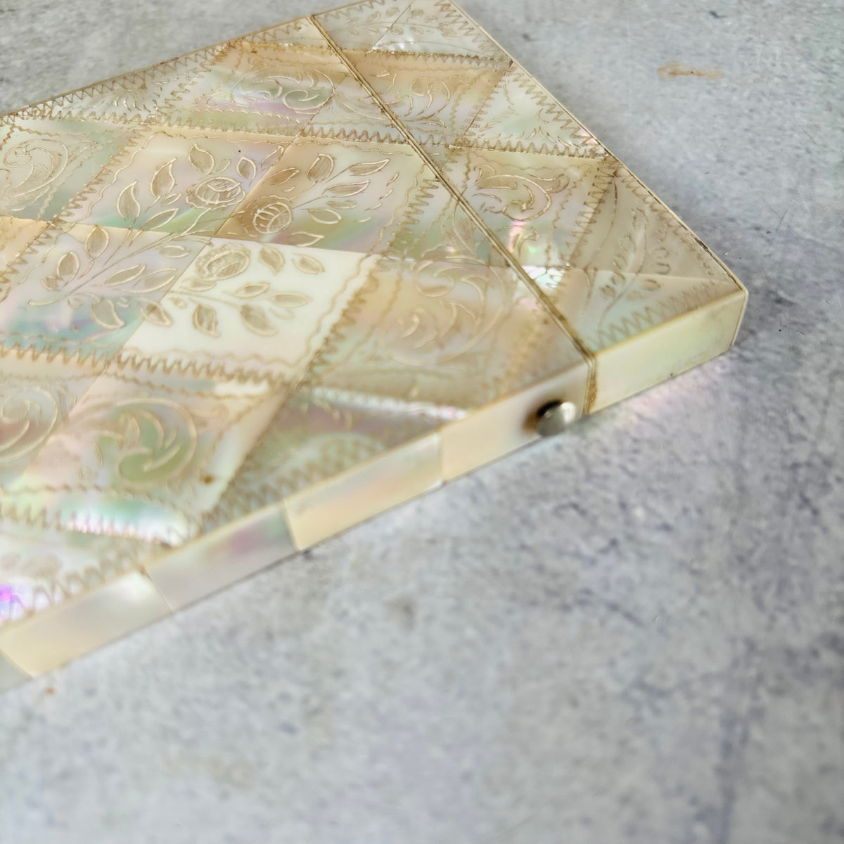 A close-up of a Rare Antique Mother Of Pearl And Sterling Silver Calling Card Case  resting on a textured gray surface.